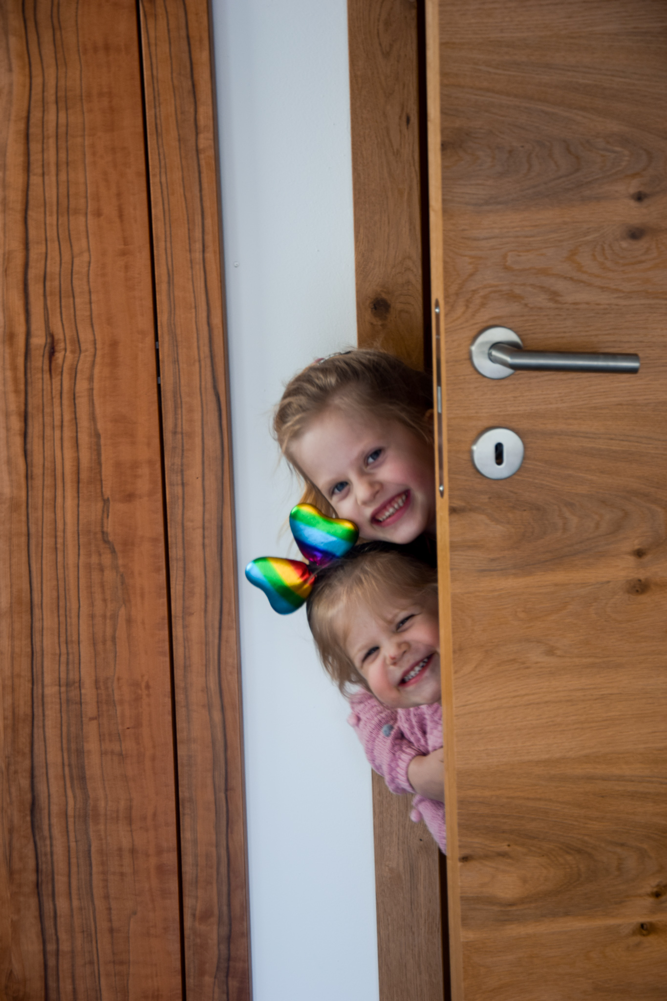 zwei Kinder blicken zwischen Tür und Türrahmen hervor